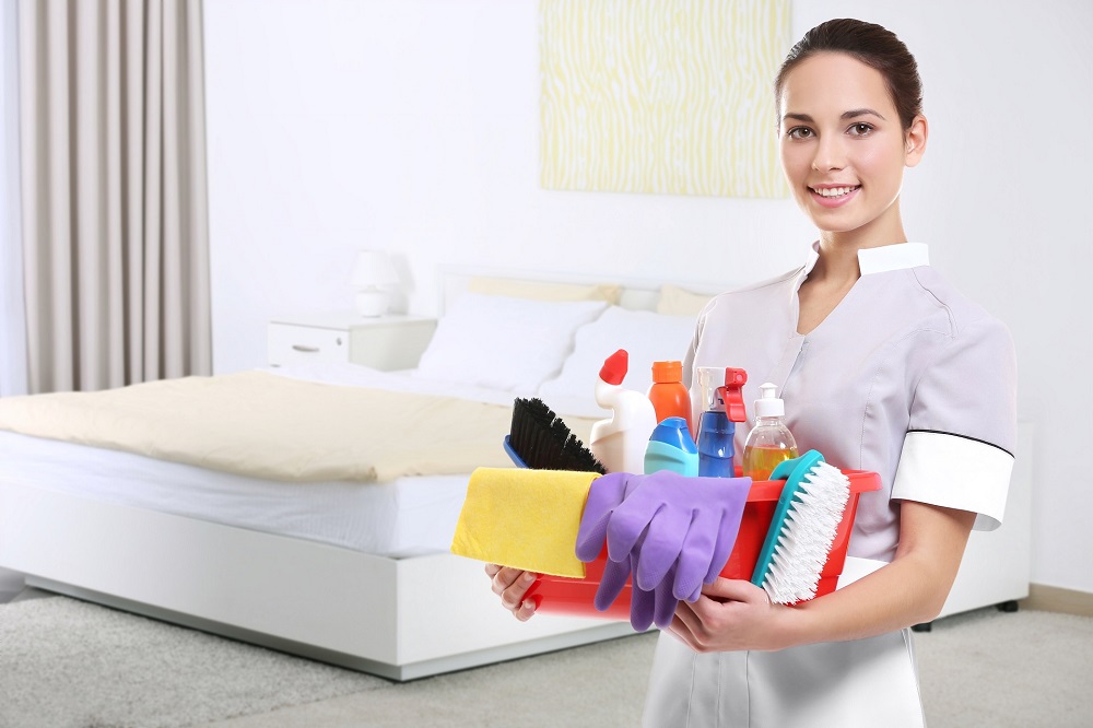 Chambermaid with cleaning equipment on bedroom background